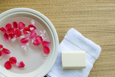Spa setting with floating rose petals, fluffy white towel, and all-natural soap bar. 