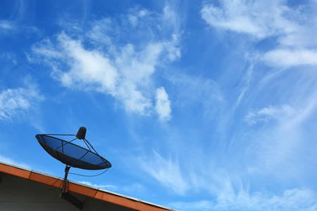 Satellite dish on roof, blue sky backgroundの写真素材