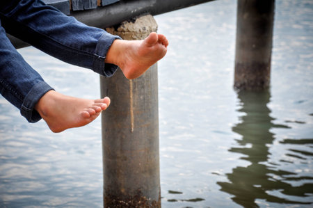 Bare feet hanging  legs into the water on wooden pierの写真素材