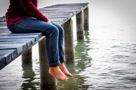 Bare feet hanging  legs into the water on wooden pierの写真素材