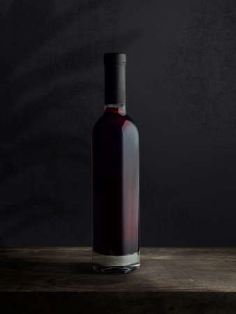 A bottle of red wine, on a wooden empty tabletop against a dark wall background. Wine bottle mockup.