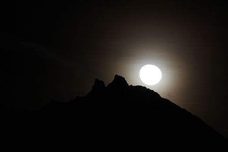 Moon shining bright behind black mountainsの写真素材