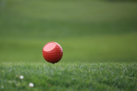 Close view of a red ball on a tee in front of a green backgroundの写真素材
