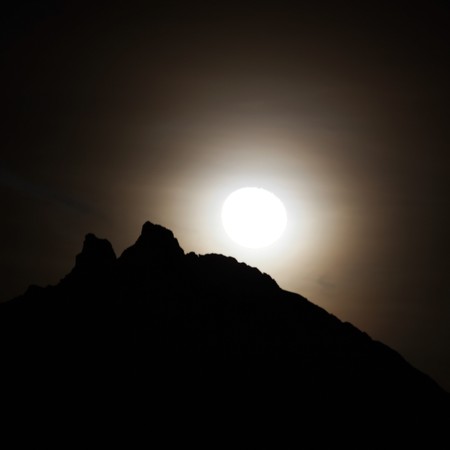 Moon shining bright behind black mountainsの写真素材