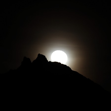 Moon shining bright behind black mountainsの写真素材