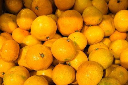 vibrant pile ripe mandarins glowing in warm light, market crate closeup showcasing dewy skin, scattered stems, glossy texture, vivid orange color, harvest abundance and commercial freshness ready for saleの写真素材