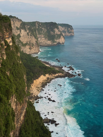 Nusa Penida, Indonesia, Pantai Atuh, rocks, ocean, balihigh cliff trail overlooking turquoise coastline, steep escarpment dotted with boulders, waves breaking on distant shoals, vegetated ledges and winding pathwayの写真素材