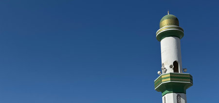 Oman, Muscat. Islamic mosque minaret with green dome against clear blue sky, copy space