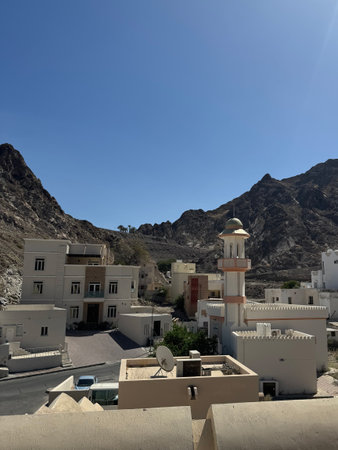 rooftop view omani mountain village mosque tower, whitewashed houses clustered against rocky slopes, clear blue sky, quiet sunlit atmosphere, local satellite dishesの写真素材