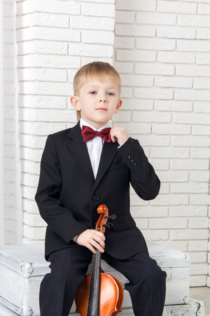little boy in a suit sitting with violin and corrects tieの写真素材