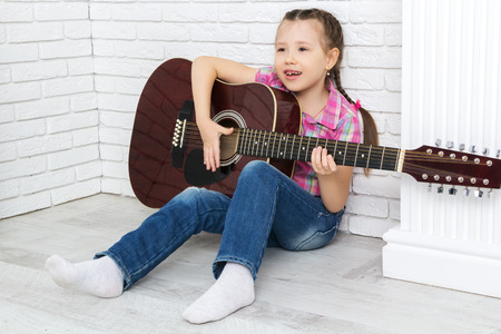 little girl playing the guitar and singing, looking away
