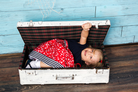 Little girl sits in a suitcase, looking at cameraの写真素材
