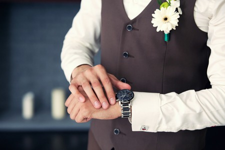 the groom in a waistcoat looks at the clock in the roomの写真素材