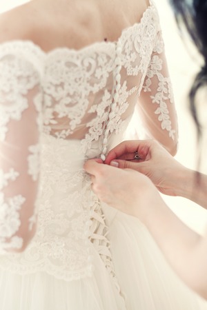 the hand of the girlfriend clasps buttons on the bride's corsetの写真素材