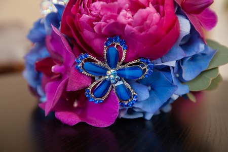 bridal bouquet from peonies of blue and red color with costume jewelry on a tableの写真素材