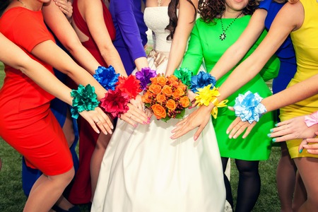 brides with an orange bouquet and bridesmaids in colourful dresses with bracelets on handsの写真素材