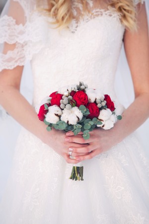 the bride holds in hand a bouquet from red peonies and cotton. Winter
