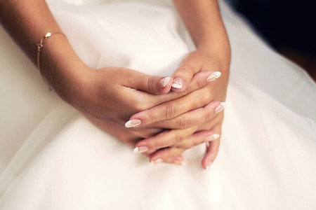 gentle hand of the bride with a beautiful manicure on a white dress close-upの写真素材