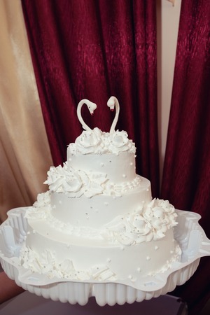 White wedding cake with a figure of a swan on a claret backgroundの写真素材