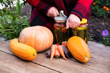 Woman in the autumn garden preserves vegetables in glass jarsの写真素材
