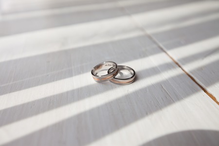 Two beautiful golden fashion wedding rings symbol of love and family jewelry standing on background of white table with gray line shadow studio closeup, horizontal pictureの写真素材