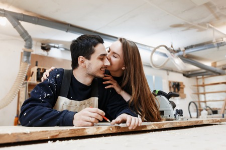 young happy family standing at a work bench in a carpentry workshop, writing a project. Family business. startup business. young specialist designer.の写真素材