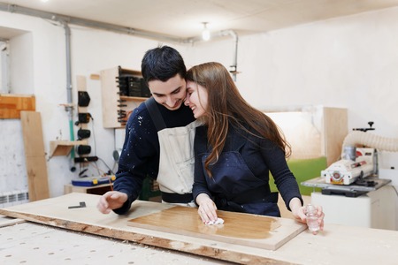 young happy family standing at a work bench in a carpentry workshop, process a tree a varnish. Family business. startup business. young specialist designer.の写真素材
