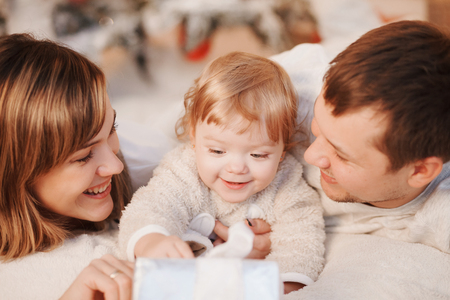 Merry Christmas and Happy Holidays! Cheerful parents and their cute daughter girls exchanging gifts. Parent and one little children having fun and playing together near Christmas tree indoors.の写真素材