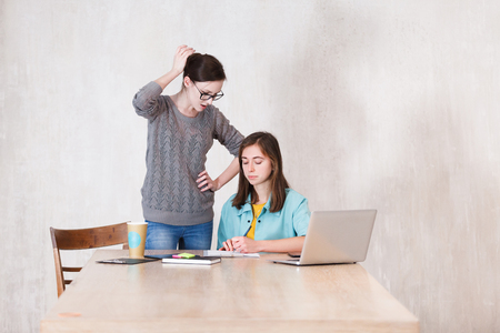 Problem is at work. Two young female managers think how to solve the problem while discussing sitting at table in the officeの写真素材