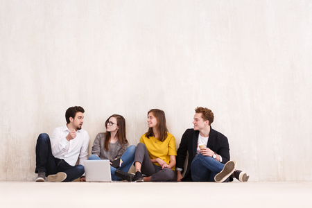 Four young office workers talking and drinking coffee while sitting on the floor during break in the creative studio copyspaceの写真素材