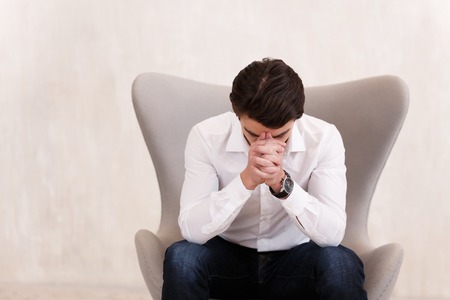 Portrait of an upset sad young man in casual clothes sitting in chair in an empty room copyspaceの写真素材