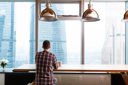 Rear view - an unidentified student in casual clothes working with computer on the background of large window overlooking the skyscrapers in the middle of the city in the business centerの写真素材