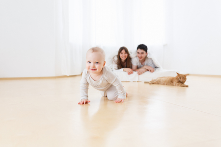 Little baby boy one-year old tried made his first step. Happy and smiling parents look behind him. Lifestyle photo of cute family in white pajamas. Family lookの写真素材
