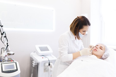 Hardware and Injections cosmetology. Process of facial beauty injections, biorevitalization of female face procedure in a beauty clinic . Cosmetologist works with patient in a white cosmetology officeの写真素材
