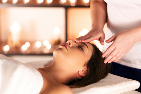 Female hands of masseuse doing massage on the head of beautiful young girl lying on massage table with closed eyes in a luxury spa resortの写真素材
