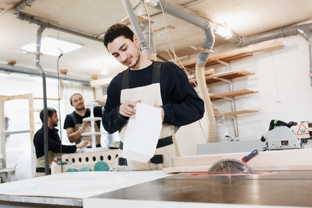 Portrait of a worker in work clothes in front of workbench tools / Portrait of man at work in workshop in garage at home. Craftsman makes own successful small business.の写真素材