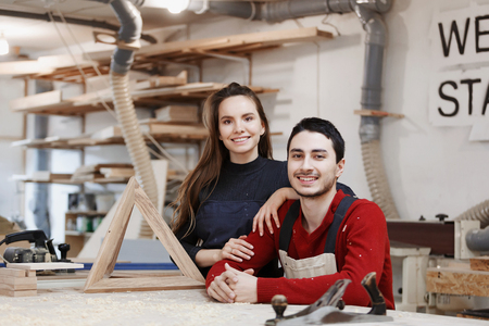 young happy family standing at a work bench in a carpentry workshop, writing a project. Family business. startup business. young specialist designer.の写真素材