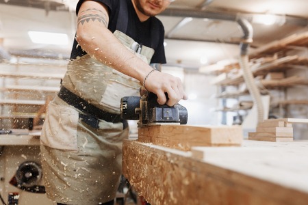 Carpenter working with electric planer on wooden plank in workshop.の写真素材