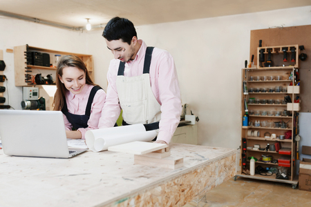 young happy family standing at a work bench in a carpentry workshop, writing a project. Family business. startup business. young specialist designer.の写真素材