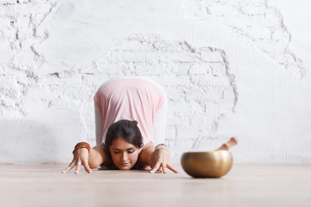 Side view - young slim brunette in leggings and top makes complex yoga exercise in light sports hallの写真素材