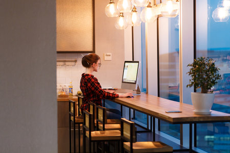 Beautiful young woman freelancer designer working behind computer in the creative office with large windows overlooking the business centerの写真素材