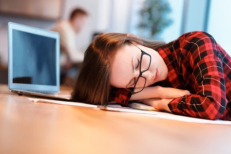 I fell asleep behind the workplace. Young tired girl manager in casual clothes asleep sitting at...