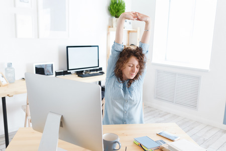 Overworked professional young female worker tired of sitting on one place, has fatigue expression release tension after long working hours in officeの写真素材