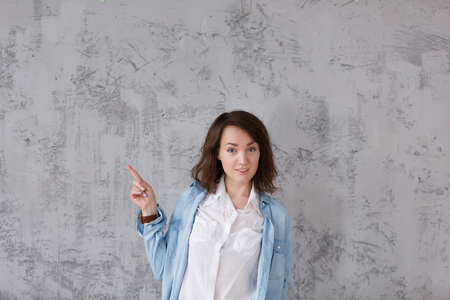 Charming positive girl in casual clothes shows something useful on gray vintage background. Copyspaceの写真素材