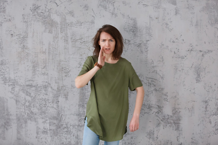 Cute young woman in an oversized green T-shirt with an angry face points to something wrong. Copyspaceの写真素材