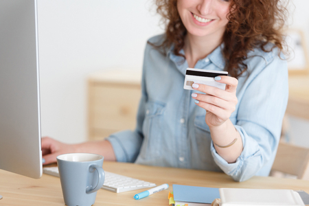 Online shopping. Cropped shot of unrecognizable caucasian female in blue shirt keyboarding on laptop pc, holding credit card,paying bills onlineの写真素材