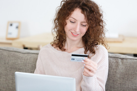 Cropped shot of caucasian female in cozy sweater sitting at home keyboarding on laptop pc, holding credit card, making payment while shopping online.の写真素材