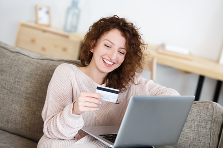 Happy and joyful redhead woman looking at credit card with happy expression, making transaction using laptop pc. Online shopping. People, business and finances concept.の写真素材