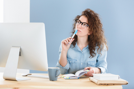 Serious hard working pleasant female freelancer thinks about the creative project, works remotely at home, looking aside with concentrated expressionの写真素材