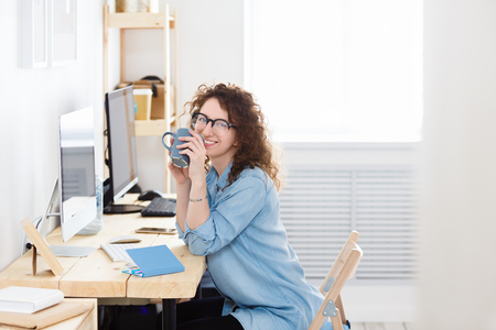 Horizontal portrait of gorgeous beautiful young successful female manager has pleasant smile reads information on laptop computer, surfes internet.の写真素材